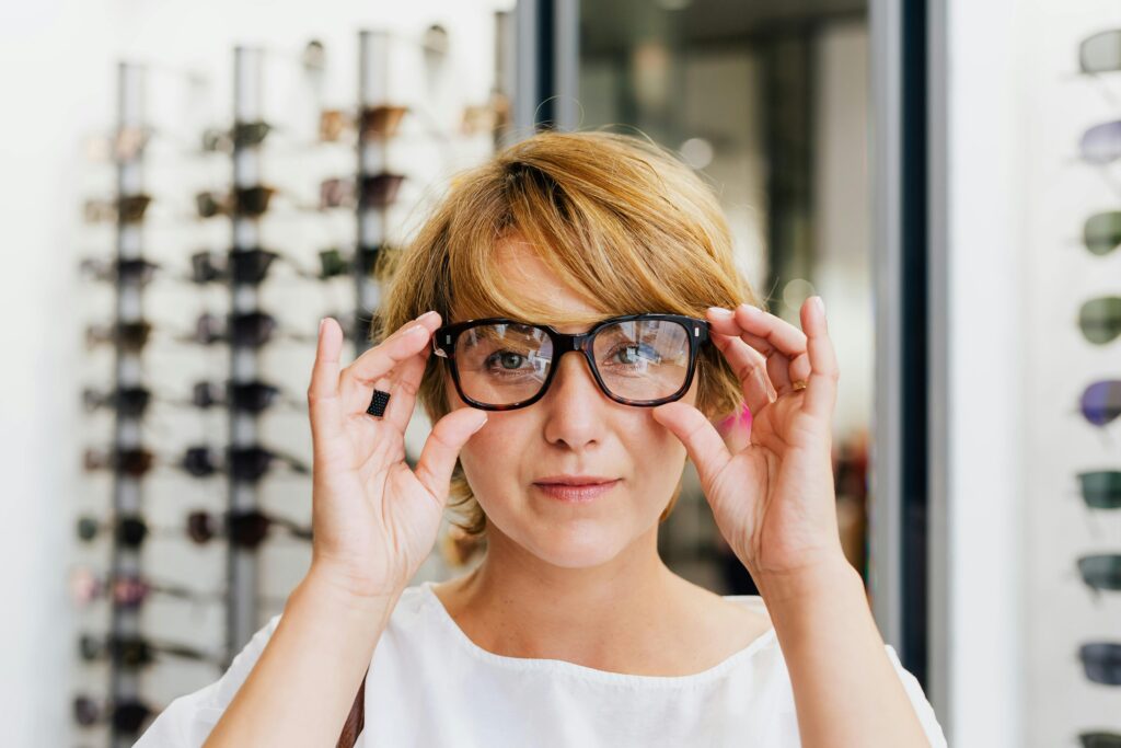 Young woman with short hair trying on glasses in an optical store, looking confident and stylish.